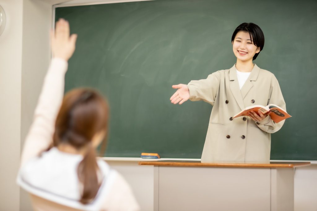 挙手をする女子中学生と、黒板の前で応える女性教師