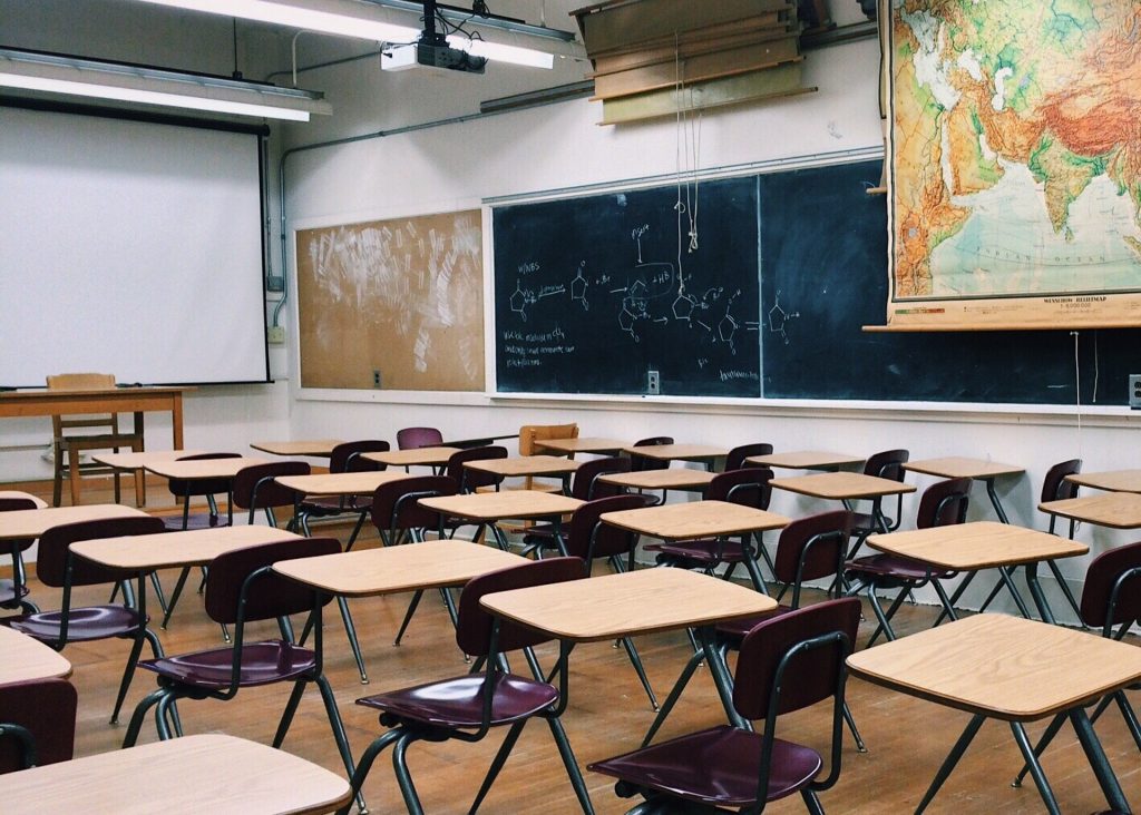 黒板の上に世界地図、教壇の前に机といすが並ぶ